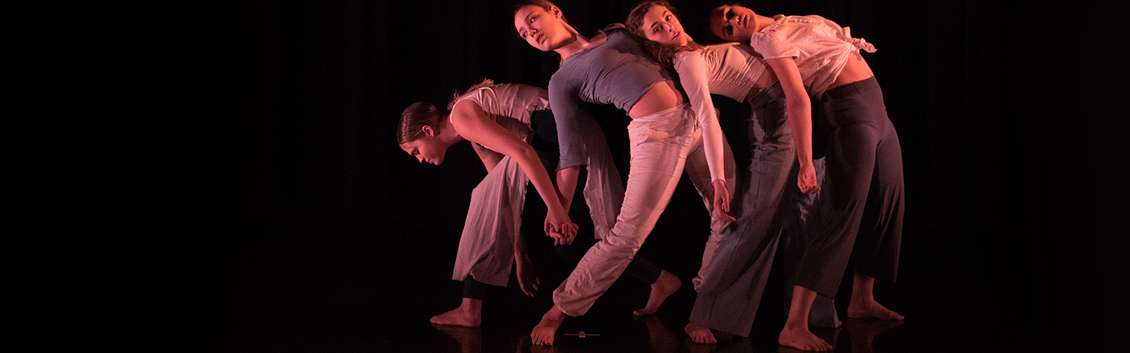 dancers in front of black backrop performing and leaning against one another